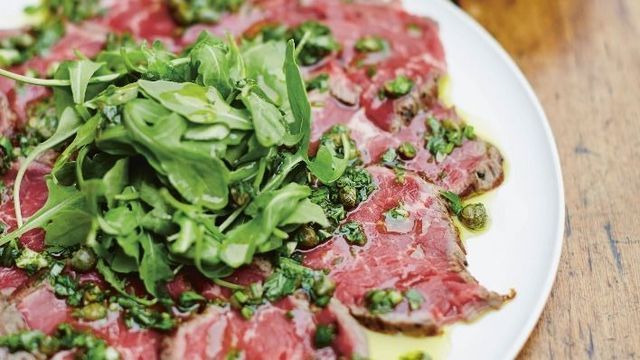 gino's italian escape carpaccio of beef with gremolata placed on large platter and dressed with rocket leaves and extra virgin olive oil