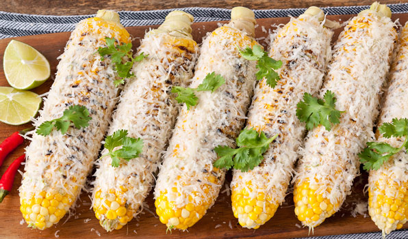 in the kitchen with stefano faita mexican grilled corn served on wooden board with lime and red chili peppers and grated parmesan cheese, parsley added on top