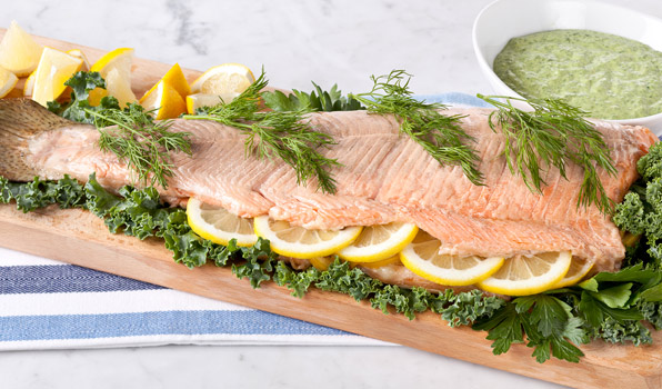 in the kitchen with stefano faita oven poached salmon with green goddess dressing on a cutting board garnished with kale leaves, lemon slices, parsley and fennel fronds